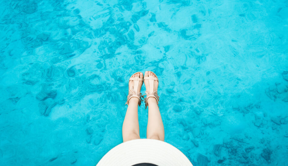 Een vrouw is aan het pootje baden in een helderblauwe zee.