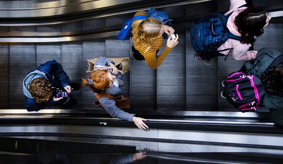 Reizigers lopen op een roltrap. Binnenkort gaat voor de trein een spitsheffing gelden.